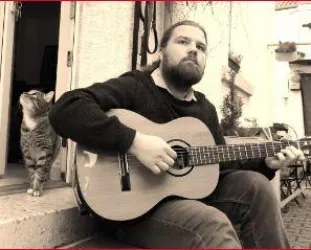 Philipp von Villiez mit seiner Gitarre sitzend auf einer Treppe, im Hintergrund eine Katze 