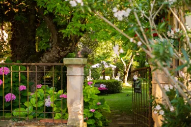 Ein schöner Garten mit grünen Pflanzen und bunten Blumen. Im Hintergrund ist ein schattiger Sitzbereich zu sehen.