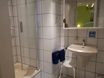 Ein modernes Badezimmer mit einer Duschkabine und einem Waschbecken. Die Wände sind mit weißen Fliesen gefliest und es gibt blaue Handtücher.