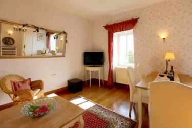 Ein gemütliches Wohnzimmer mit einem stilvollen Tisch und einem Fernseher. Die Wände sind in sanften Farben gestaltet, und große Fenster sorgen für viel Licht.