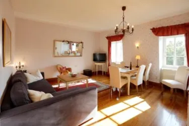 Ein gemütliches Wohnzimmer mit einem grauen Sofa und einem Essbereich. Große Fenster bringen viel Licht in den Raum.