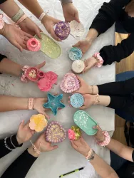 Bunte und kreative Formen aus Seife, umgeben von mehreren Händen. Die Farben sind lebhaft und die Anordnung wirkt einladend und fröhlich.