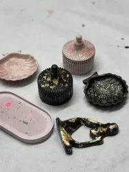 Ein Set von dekorativen Schalen und Boxen in verschiedenen Farben und Formen. Einige sind mit goldenen Akzenten verziert und liegen auf einer hellen Oberfläche.