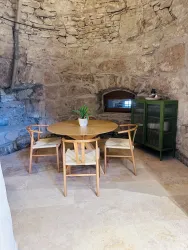 Ein gemütlicher Essbereich mit einem runden Holztisch und vier Stühlen. Die Wände sind aus Naturstein und der Raum hat ein rustikales Ambiente.