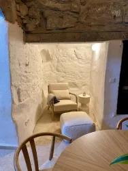 Ein gemütlicher Raum mit einem bequemen Sessel und einem kleinen Tisch. Die Wände sind aus hellem Stein und es gibt sanfte Beleuchtung.