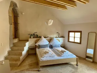 Ein gemütliches Schlafzimmer mit einem Doppelbett, modernos Design und einer warmen Atmosphäre. Im Raum befinden sich ein Spiegel und eine Treppe, die zu einem weiteren Bereich führt.