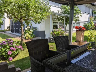 Ein schöner Garten mit blühenden Blumen und einem Tisch aus Glas. Im Hintergrund ist ein modernes Haus zu sehen.