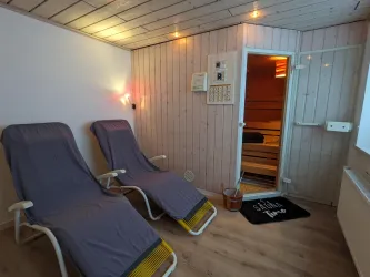 Ein entspannender Raum mit zwei Liegen und sanfter Beleuchtung. Im Hintergrund befindet sich eine Sauna, die zum Relaxen einlädt.