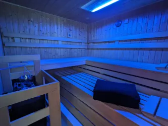 Eine moderne Sauna mit Holzverkleidung und blauer Beleuchtung. Auf den Bänken liegt ein Handtuch bereit.