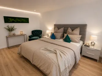 Ein modernes Schlafzimmer mit einem großen Bett und gemütlichen Kissen. Grüner Sessel und stilvolle Beleuchtung sorgen für eine einladende Atmosphäre.