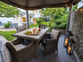 Eine gemütliche Terrasse mit einem Tisch, auf dem Wein und Snacks stehen. Umgeben von grünem Garten und stimmungsvoller Beleuchtung.