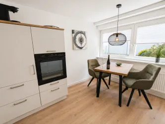 Eine moderne Küche mit einem Holz-Tisch und zwei Stühlen. Der Raum ist hell und freundlich mit einem Fenster, das nach draußen blickt.