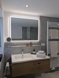 Ein modernes Badezimmer mit einem stilvollen Waschbecken und einem beleuchteten Spiegel. Handtücher sind ordentlich auf einem Heizkörper platziert.
