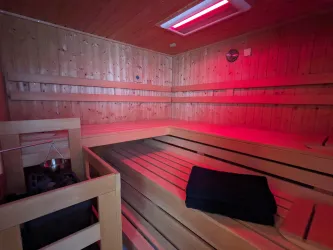 Ein ruhiger Sauna-Raum mit Holzverkleidung und einer roten Beleuchtung. Auf einer der Bänke liegt ein schwarzes Handtuch.