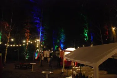 Ein bunt beleuchtetes Waldstück, ausgestattet mitr einem großen, weißem Zelt und Stühlen.