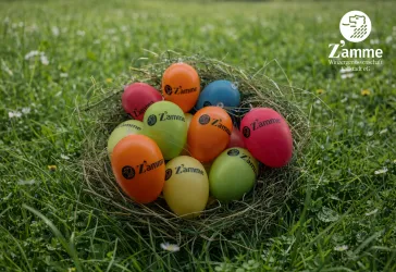 Bunte Ostereier liegen in einem Nest aus Gras. Die Eier sind mit dem Logo der Winzergenossenschaft Zamme versehen.
