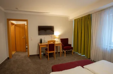 <p>Blick vom Bett in Richtung Tür, auf einen Fernseher, Schrank und einen Schreibtisch</p>