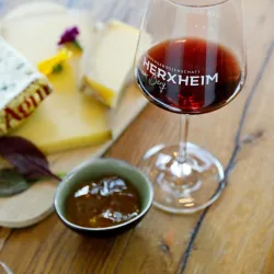 <p>Ein Holztisch mit einemr Käsetellerr und einem Glas Rotwein der Winzergenossenschaft Herxheim/Bg.</p>