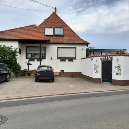 Ein modernes Gästehaus mit rotem Dach und einem gepflegten Außenbereich. Vor dem Haus ist ein Parkplatz mit einem schwarzen Auto.