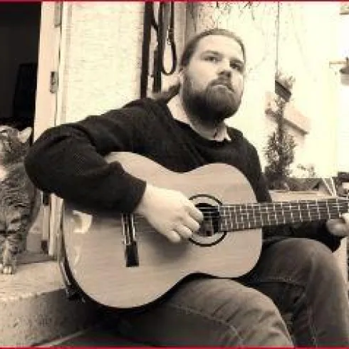 Philipp von Villiez mit seiner Gitarre sitzend auf einer Treppe, im Hintergrund eine Katze 