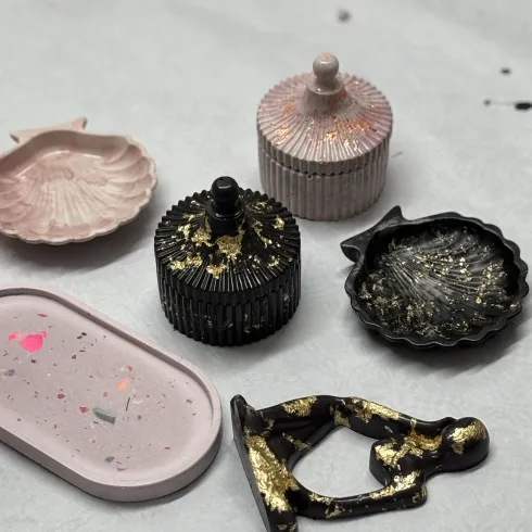 Ein Set von dekorativen Schalen und Boxen in verschiedenen Farben und Formen. Einige sind mit goldenen Akzenten verziert und liegen auf einer hellen Oberfläche.