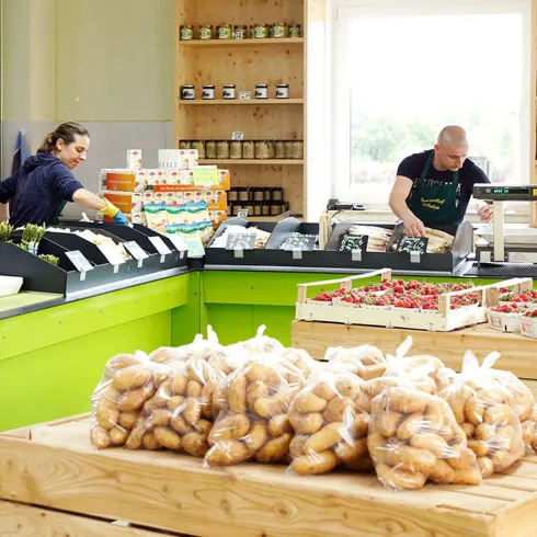 Der modern gestaltete Hofladen des Spargelhofs. Zu sehen ist eine grüne Theke mit Verkäufer und gefüllte Tische, Regale.