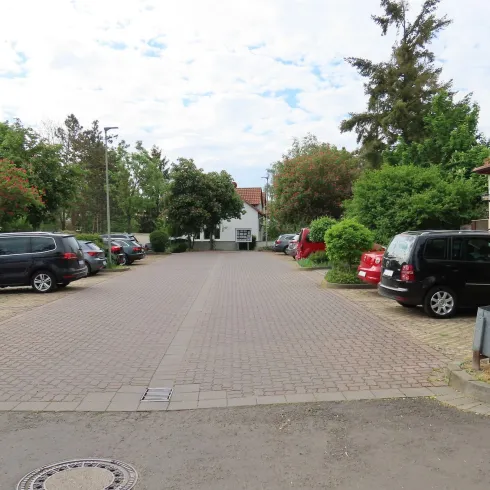 Ein Mittelgroßer Prkplatz der gepflastert ist. Schhon einige Autos parken darauf , jedoch ist noch Platz für weitere. 