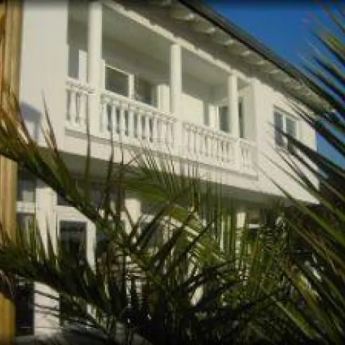 Ein modernes Gebäude mit weißen Wänden und Balkonen. Palmenblätter im Vordergrund verleihen der Szene einen tropischen Look.