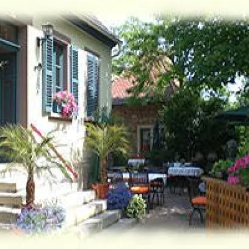 Gemütlicher Außenbereich des Restaurants mit Tischen und Stühlen. Umgeben von bunten Blumen und grünem Laub.