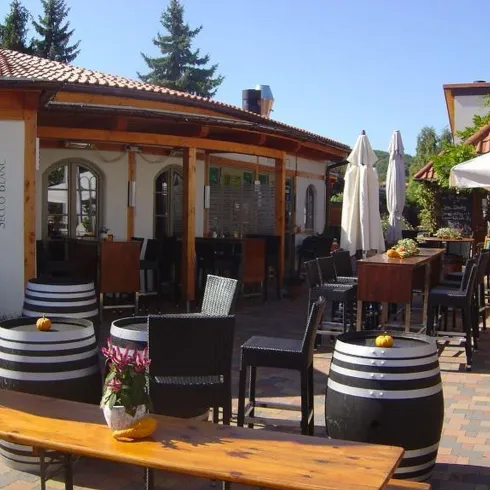 Die Secco- HÜtte von außen. Vor der Hütte ist eine gepflasterte Terasse mit Sitzmöbeln und Weinfässerals Deko.