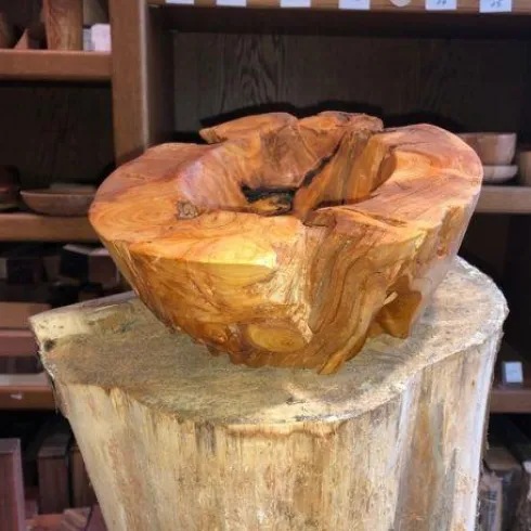 <p>Gedrechselte Holunderholzschale auf einer Holzsäule. Im Hintergrund Regale mit verschieden gedrechselten Holzschalen.